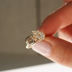 a woman's hand holding an engagement ring with two diamonds on top of it