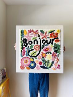 a person holding up a painting with the word bonjou written in floral designs on it