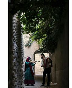 a man and woman standing in an alley with trees on either side, one playing the accordion