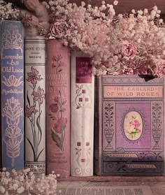 several books are lined up on a shelf with flowers in the corner and one is empty