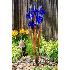 blue glass flowers are in the middle of a rock and grass garden with bamboo fence behind it