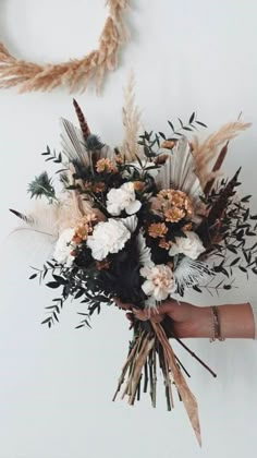 a person holding a bouquet of flowers in their hand and two wreaths on the wall behind them