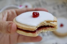 a hand holding a jelly filled pastry with white frosting and cherries on top