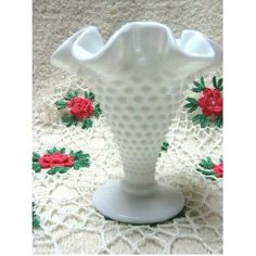 a white vase sitting on top of a table next to a doily covered cloth