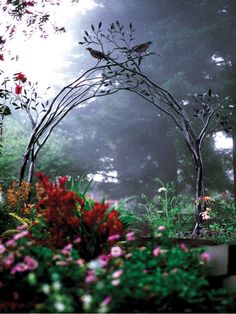 a bird sitting on top of a metal arch in the middle of a garden filled with flowers