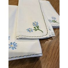 three white napkins with blue flowers on them sitting on a wooden floor next to each other