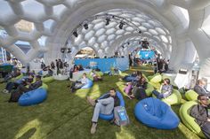 many people are sitting on bean bags in an open area with green grass and white walls