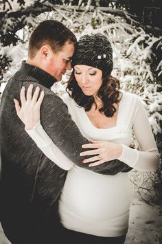 a pregnant couple cuddling in the snow