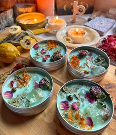 four tins filled with flowers sitting on top of a wooden table next to candles