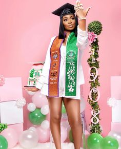 a woman wearing a graduation cap and gown holding up a green scarf in front of balloons