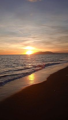 the sun is setting over the water at the beach with waves coming in to shore