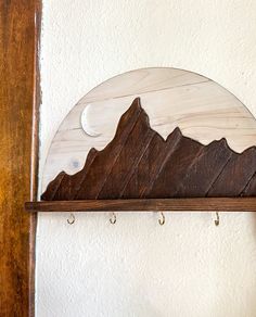 a wooden shelf with two hooks on it and a mountain scene hanging from the wall