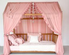 a canopy bed with pink curtains and pillows on it's sides, in front of a white wall