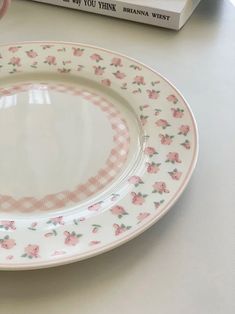 a white plate with pink flowers on it next to a stack of books and a cup