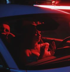 a woman sitting in the driver's seat of a car at night with her phone up to her ear