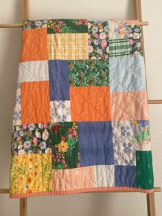 an orange and blue patchwork quilt hanging on a wall next to a wooden ladder