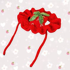 a crocheted red hat with a green leaf on it and hearts in the background