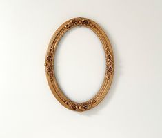 an oval gold frame on a white wall with flowers in the center and leaves at the bottom