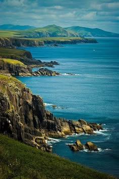 an ocean view with cliffs and green grass on the side, blue water in the foreground