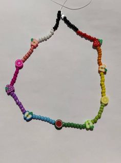 a multicolored beaded necklace hanging from a hook on a white surface with an object in the background