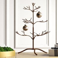 a metal christmas tree with two ornaments on it's branches, next to a potted plant