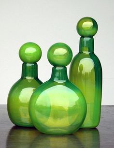 three green glass vases sitting on top of a wooden table next to each other