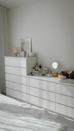 a bedroom with white dressers and various items on the top shelf, along with a large window