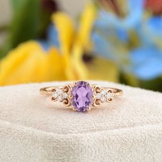 a ring with an amethyst purple stone surrounded by three diamonds on a white surface