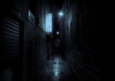 a dark alley way with a hotel sign lit up at the end in the distance