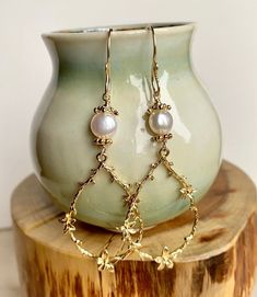 Enhance your boho chic style with this set of long gold teardrop-shaped flower branch dangly earrings. Featuring large gold-plated brass flower branch charms, these earrings are delicately crafted and exude a sweet charm. The handmade earring hooks, crafted with 10K gold-filled wire, add a touch of elegance. At the top, white freshwater pearls with gold-plated floral bead caps provide a classic and timeless accent. Measuring 2 1/2" X 7/8", including the gold-filled wire hooks, these earrings are Gold Feminine Dangle Flower Earrings, Dainty Pearl Drop Dangle Flower Earrings, Elegant Handmade Teardrop Flower Earrings, Whimsical Gold Flower Earrings For Wedding, Elegant Handmade Flower Teardrop Earrings, Elegant Handmade Flower Shaped Teardrop Earrings, Dainty Flower Dangle Earrings With Pearl Drop, Handmade Elegant Flower Teardrop Earrings, Gold Flower Chandelier Earrings Elegant Style