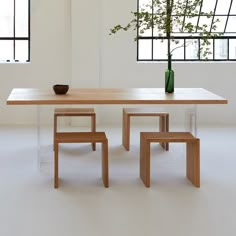 a wooden table with two chairs and a vase on it, in front of windows