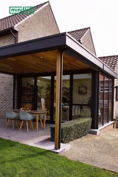 a covered patio with chairs and table in front of brick building on grass lawn area