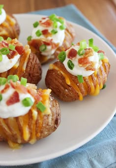 small potatoes topped with bacon, cheese and green onions on a white plate next to a blue napkin