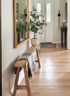 a wooden bench sitting in front of a mirror next to a white door with plants on it