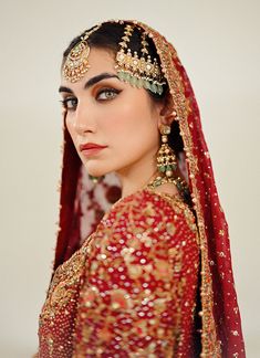 a woman in a red and gold bridal outfit with jewelry on her head, looking off to the side