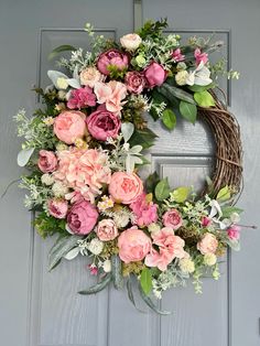 a wreath with pink flowers and greenery hangs on a gray front door as if it were painted