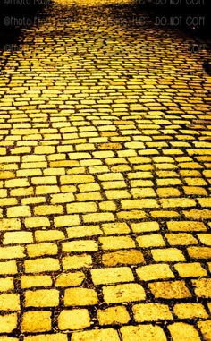 an old cobblestone street with yellow light reflecting off the wet pavement and trees in the background