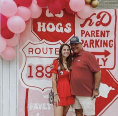 a man and woman standing in front of a sign with balloons on the wall behind them