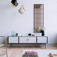 a living room with white furniture and two lamps hanging from the ceiling, along with a large mirror on the wall