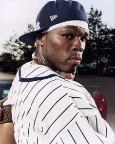 a man in a baseball uniform standing next to a car and looking at the camera