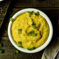 a white bowl filled with hummus and green onions on top of a wooden table