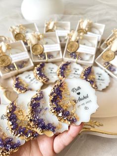 purple and gold decorated cookies are displayed on a platter with white boxes in the background