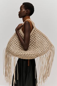 a woman wearing a large woven bag with fringes on her shoulders and shoulder, standing in