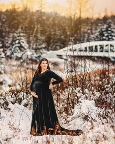 a pregnant woman standing in the snow with her hands on her hips wearing a black dress