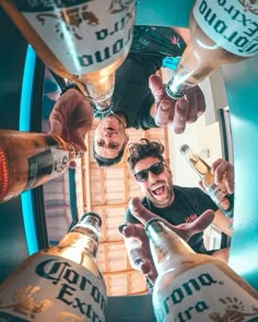 three men are standing in a circle holding beer bottles and pointing at the camera with their thumbs up