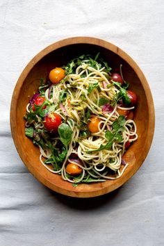 a wooden bowl filled with pasta and veggies on top of a white table