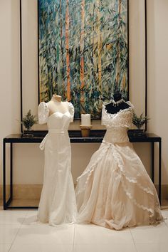 two wedding dresses are on display in front of a painting and vases with candles