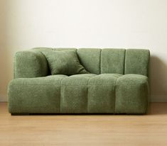 a green couch sitting on top of a hard wood floor next to a white wall