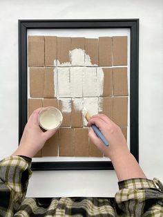 a person is holding a paintbrush and painting on a piece of cardboard that has been taped to the wall