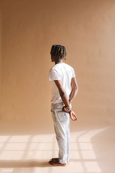 a man with dreadlocks standing in front of a beige wall looking at something